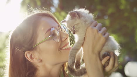 Close-up-view-of-a-caucasian-woman-in-glasses-holding-small-cat-and-kissing-it-in-the-park-on-a-summer-day