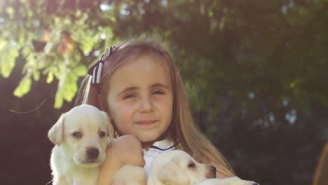 Close-up-view-of-cute-caucasian-girl-holding-small-labrador-puppies-in-the-park-on-a-summer-day