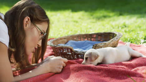 Caucasian-woman-playing-with-a-cute-labrador-puppy-on-a-blanket-on-the-grass-in-the-park-on-a-summer-day