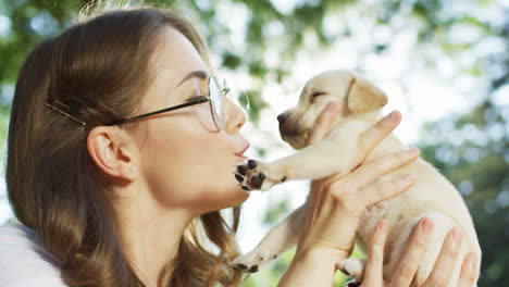 Close-up-view-of-caucasian-woman-holding-labrador-puppy-and-kissing-it-in-the-park-on-a-summer-day