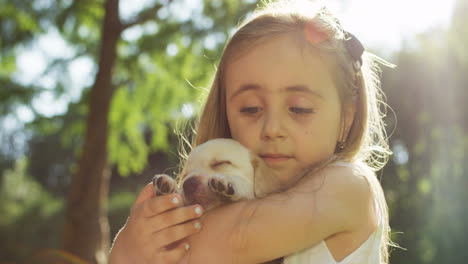 Close-up-view-of-a-caucasian-little-girl-holding-a-small-labrador-puppy-while-looking-at-camera-in-the-park-on-a-summer-day