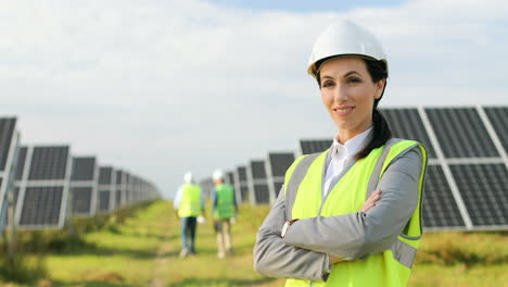 Portrait-of-beautiful-female-engineer-in-protective-helmet-and-uniform-with-arms-crossed-smiling-at-camera-on-solar-plantation