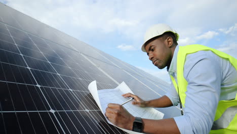 Seitenansicht-Eines-Jungen-Afroamerikanischen-Ingenieurs,-Der-Sich-Notizen-Zu-Einem-Projekt-Auf-Einem-Solarpanel-Macht