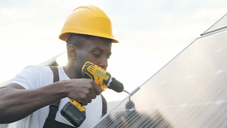 Close-up-view-of-african-american-man-in-special-uniform-and-protective-helmet-repairing-a-solar-panel
