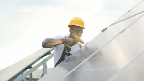 Hombre-Afroamericano-Con-Uniforme-Especial-Y-Casco-Protector-Reparando-Un-Panel-Solar