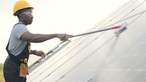 Hombre-Afroamericano-Con-Uniforme-Especial-Y-Casco-Protector-Limpiando-Un-Panel-Solar