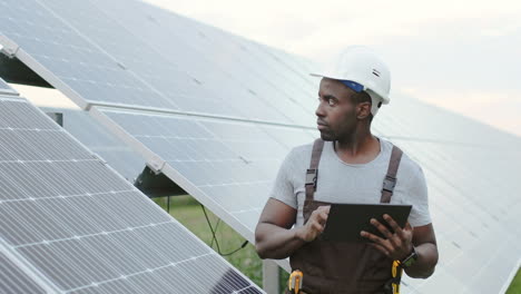 Joven-Ingeniero-Afroamericano-Parado-Afuera-Cerca-De-Paneles-Solares-Y-Usando-Una-Tableta