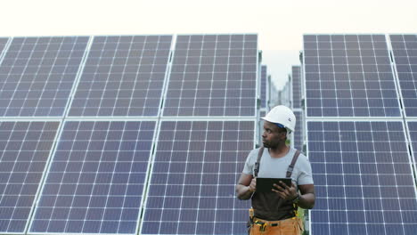 Young-african-american-male-engineer-standing-outside-near-solar-panels-and-using-a-tablet