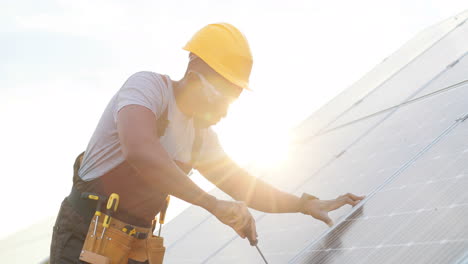 African-american-man-in-special-uniform-and-protective-helmet-repairing-a-solar-panel
