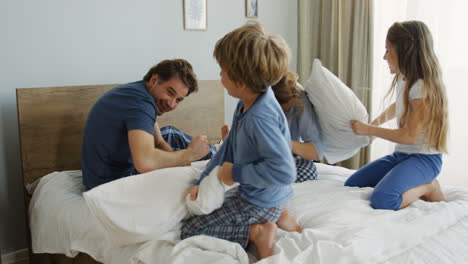 Cute-little-children-having-fun-and-fighting-with-pillows-with-their-parents-in-bed-with-pillows-in-the-morning