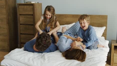 Happy-friendly-family-having-fun-while-they-are-lying-and-playing-and-tickling-on-the-bed-in-the-morning-of-the-weekend-day