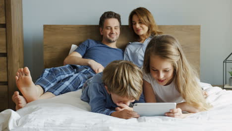 Close-up-view-of-a-little-girl-and-her-brother-lying-on-the-bed-and-watching-something-on-the-tablet