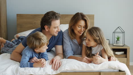 Cheerful-parents-and-their-sons-lying-on-the-bed-and-talking-in-the-morning