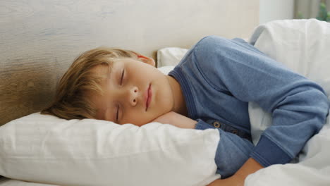 Close-up-view-of-cute-small-blond-boy-sleeping-on-the-bed-in-the-morning