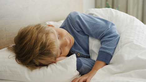 Close-up-view-of-cute-small-blond-boy-sleeping-on-the-bed-in-the-morning