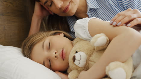 Close-up-view-of-cute-blonde-little-girl-sleeping-on-the-bed-while-hugging-her-teddy-bear