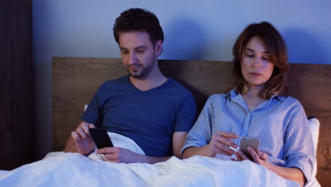 Caucasian-couple-sitting-on-the-bed-and-using-smartphones,-then-they-say-goodnight-to-their-sons