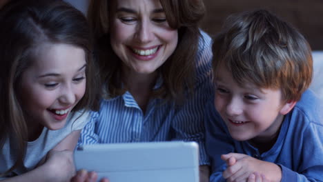 Close-up-view-of-caucasian-mother-and-his-little-son-and-daughter-lying-on-the-bed-and-watching-something-on-the-tablet