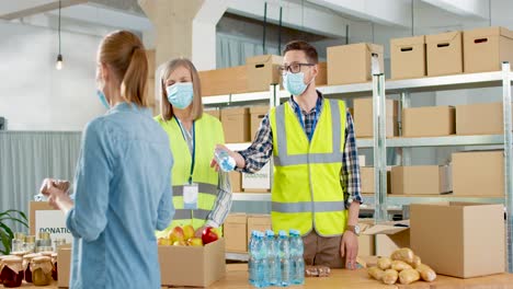 Caucasian-young-male-and-senior-female-volunteers-in-facial-mask-giving-food-and-water-to-homeless-people-in-charity-warehouse