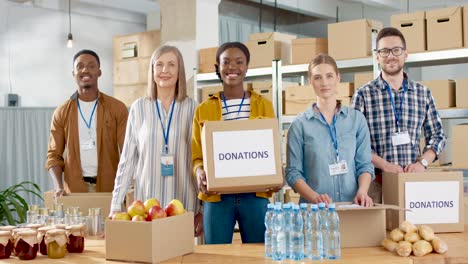 Multiethnische-Gruppe-Von-Freiwilligen,-Die-Kisten-Mit-Lebensmitteln-Und-Kleidung-In-Einem-Wohltätigkeitslager-Packen-Und-In-Die-Kamera-Lächeln