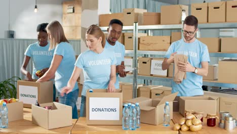Multiethnische-Gruppe-Von-Freiwilligen,-Die-Kisten-Mit-Lebensmitteln-Und-Kleidung-In-Einem-Wohltätigkeitslager-Packen
