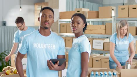 Afroamerikanische-Junge-Männliche-Und-Weibliche-Freiwillige,-Die-Auf-Dem-Tablet-Tippen-Und-In-Die-Kamera-Lächeln