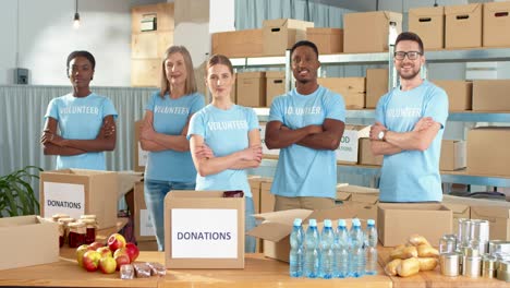 Multiethnic-group-of-volunteers-standing-in-charity-warehouse-and-smiling-to-the-camera