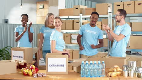 Multiethnic-group-of-volunteers-standing-in-charity-warehouse-clapping-hands-and-giving-high-five-in-charity-warehouse