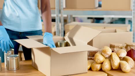Close-up-view-of-african-american-volunteer-hands-packing-box-with-cans-of-preserves-in-charity-warehouse