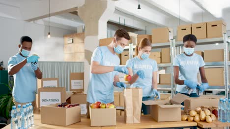 Multiethnic-group-of-volunteers-in-facial-mask-packing-boxes-with-food-and-clothes-in-charity-warehouse