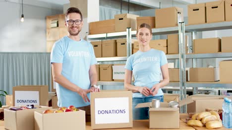 Caucasian-young-male-and-female-volunteers-packing-box-with-food-and-then-smiling-to-the-camera-in-charity-warehouse