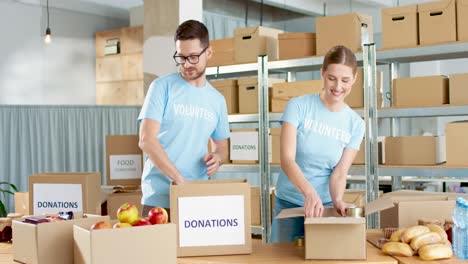Caucasian-young-male-and-female-volunteers-packing-box-with-food-in-charity-warehouse