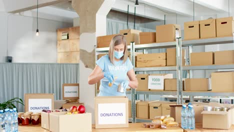 Caucasian-woman-volunteer-in-facial-mask-packing-donation-boxes-in-charity-warehouse
