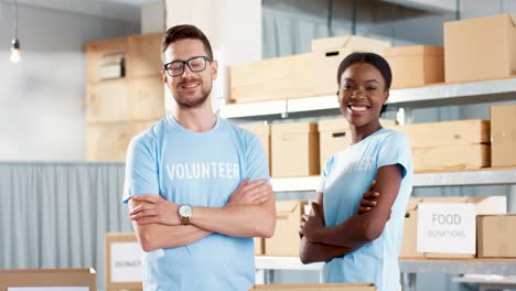 Caucasian-man-and-young-African-American-female-volunteer-standing-in-warehouse-looking-at-camera-and-smiling-in-good-mood