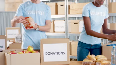 Caucasian-man-and-young-African-American-female-volunteer-packing-donation-boxes-with-food-in-charity-warehouse