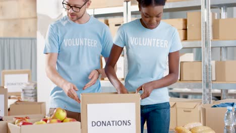 Kaukasischer-Mann-Und-Junge-Afrikanisch-amerikanische-Freiwillige-Packen-Spendenboxen-Mit-Lebensmitteln-Im-Lager-Für-Wohltätigkeitszwecke