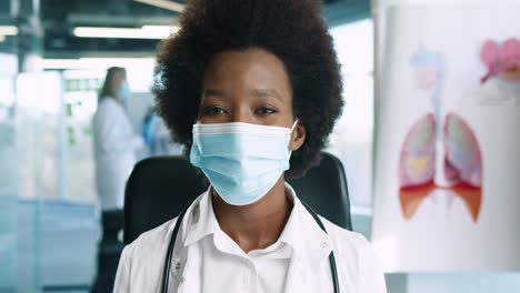 Close-up-view-of-African-American-female-doctor-in-medical-mask-looking-at-camera-in-good-mood-in-hospital