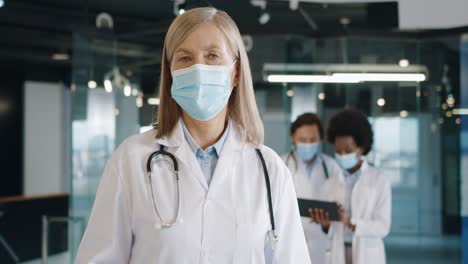 Close-up-view-of-caucasian-female-doctor-in-medical-mask-looking-at-camera-standing-in-hospital