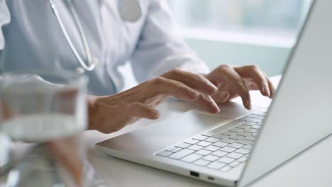 Close-up-view-of-senior-Caucasian-female-doctor-hands-typing-on-laptop-at-desktop