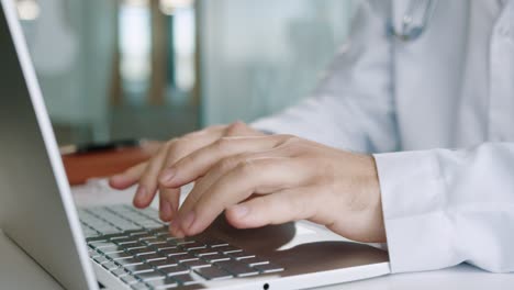 Close-up-view-of-senior-Caucasian-male-doctor-hands-typing-on-laptop-at-desktop