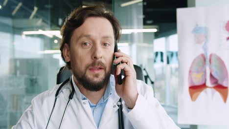 Close-up-view-of-caucasian-senior-male-doctor-with-stethoscope-sitting-at-desk-and-talking-on-the-phone-in-hospital