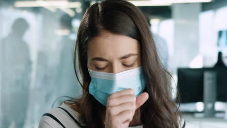 Close-up-view-of-Caucasian-young-female-patient-wearing-medical-mask-and-coughing-badly-while-talking-indoor-in-hospital