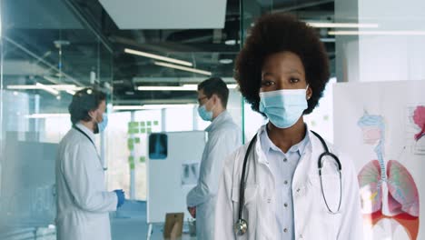 Kaukasische-Afrikanisch-amerikanische-Ärztin-In-Medizinischer-Maske,-Die-Im-Krankenhausbüro-In-Die-Kamera-Blickt