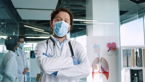 Caucasian-male-doctor-wearing-medical-mask-looking-at-camera-in-hospital-office