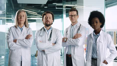 Multiethnisches-Ärzteteam-In-Weißen-Kitteln,-Die-Gut-Gelaunt-In-Die-Kamera-Schauen,-Während-Sie-Im-Krankenhauskorridor-Stehen