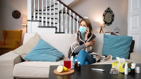 Sick-woman-wearing-a-medical-mask-sitting-on-the-sofa-and-talking-on-cellphone