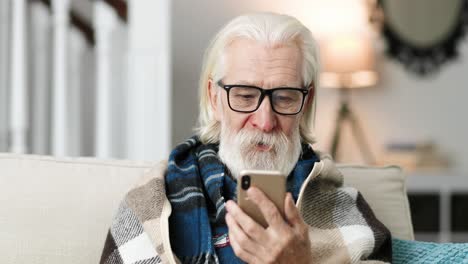 Close-up-portrait-of-old-man-wearing-glasses,-sittiing-and-video-chatting-on-cellphone