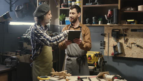 Two-carpenters-standing-in-workshop-and-watching-some-video-on-tablet-in-carpentry-workshop