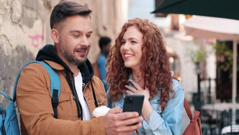 Caucasian-man-with-beard-and-caucasian-woman-watching-something-in-a-smartphone-in-the-street