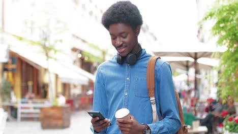 Hombre-Afroamericano-Sosteniendo-Café-Para-Llevar-Y-Usando-Un-Teléfono-Inteligente-En-La-Calle